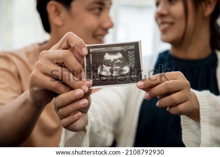 Happiness of a pregnant woman and her husband in the bedroom with the ultrasound film of the fetus that shows the results that the child is healthy. Concept of preparing for a family and succession.
