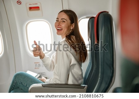 Cheerful young woman doing thumbs up gesture in plane Royalty-Free Stock Photo #2108810675
