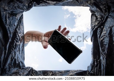 a man throws a non-working smartphone into a trash can. Bottom view from the trash can. The problem of recycling and pollution of the planet with garbage. Royalty-Free Stock Photo #2108810975