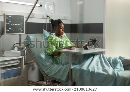 African american young patient lying in bed recovering after medical surgery watching online cartoons on tablet computer during clinical appointment in hospital ward. Medicine service