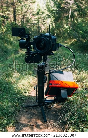 Professional DSLR Camera on 3-axis Gimbal Stabilization Device in Forest. Cinematographer Operator. Slow Motion Royalty-Free Stock Photo #2108825087