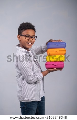 Joyous schoolboy demonstrating his food containers before the camera