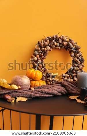 Beautiful acorn wreath, pumpkins and candles near orange wall