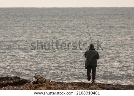 a male fisherman with a black raincoat catches fish on the sea in the winter season