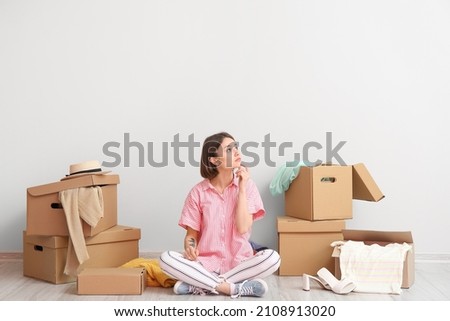 Thoughtful young woman with wardrobe boxes and things near light wall Royalty-Free Stock Photo #2108913020