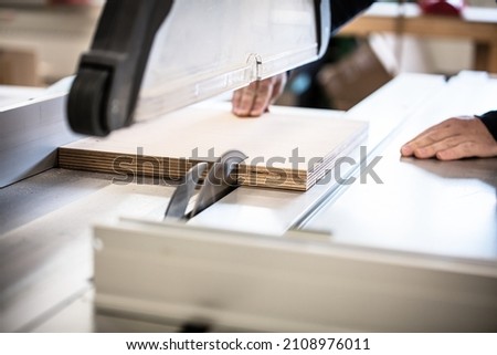 male craftsman saws wood on a circular saw, carpenter saws wood on a table saw in his workshop Royalty-Free Stock Photo #2108976011