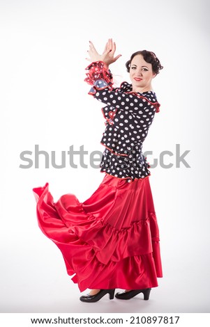 young beautiful brunette female spanish flamenco dancer in black shirt and red flamenco skirt dancing with her arms and flying red skirt in studio on gray background