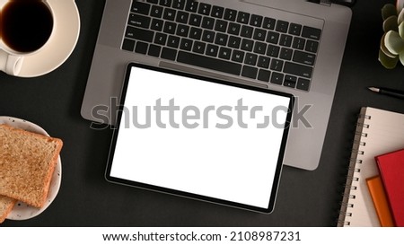 Mockup screen of a digital tablet computer on laptop computer over modern black workspace design.