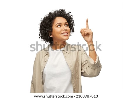 people, ethnicity and portrait concept - happy smiling woman in shirt pointing finger up over white background