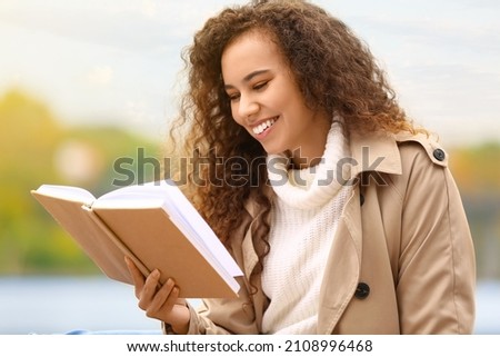 Beautiful African-American woman reading book outdoors