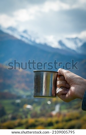 Close-up of a woman's hand holding a metal cup with coffee or tea against the background of mountains. Concept of travel, camping, active lifestyle. Vertical photo