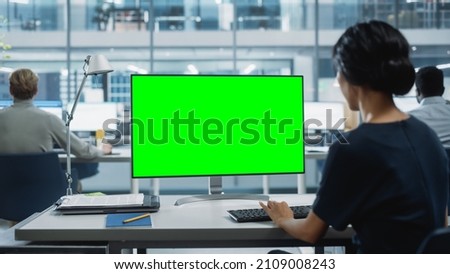 Close Up Over the Shoulder Shot of a Businesswoman Working on Desktop Computer with Chroma Key Green Screen Mock Up Display. Digital Projects Manager Typing Data, Using Keyboard and Mouse.