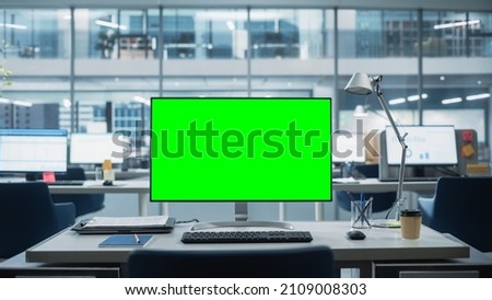 Desktop Computer Monitor with Mock Up Green Screen Chroma Key Display Standing on the Desk in the Modern Business Office. In the Background Glass Wall with Big City Office. Royalty-Free Stock Photo #2109008303