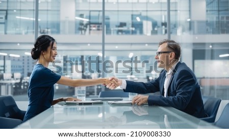 Multiethnic Diverse Office Conference Room Meeting: Two Creative Entrepreneurs Shake Hands after Signing Contract. Stylish Young Businesspeople work on Digital e-Commerce Startup Project.