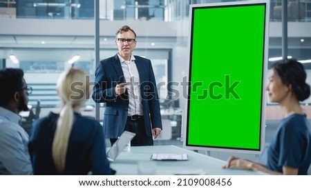 Company Operations Manager Holds Meeting Presentation for a Team of Economists. Adult Male Uses Digital Whiteboard with Vertical Green Screen Mock Up Display. People Work in Business Office.
