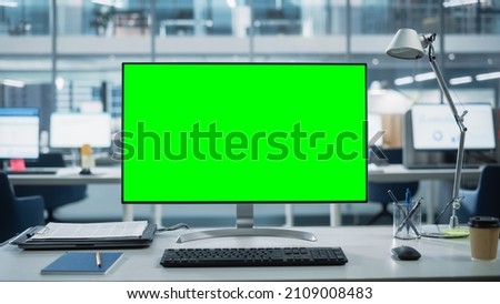 Desktop Computer Monitor with Mock Up Green Screen Chroma Key Display Standing on the Desk in the Modern Business Office. In the Background Glass Wall with Big City Office. Royalty-Free Stock Photo #2109008483