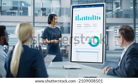 Female Operations Manager Holds Meeting Presentation for a Team of Economists. Asian Woman Uses Digital Whiteboard with Growth Analysis, Charts, Statistics and Data. People Work in Business Office. Royalty-Free Stock Photo #2109008501