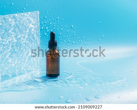A bottle with a pipette, a cosmetic product, splashes and drops of water on a blue background Royalty-Free Stock Photo #2109009227