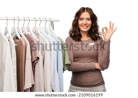 sale, shopping and business concept - happy female shop assistant or saleswoman with clothes on hanger over white background