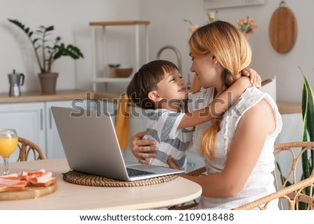Little boy hugging his mother at dining table in kitchen