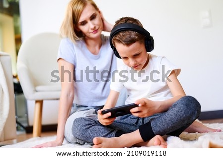 Child boy with mother holds phone is lying on the floor with headphones watching cartoons, listening to music, playing games