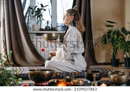 Sound healing with singing bowls, vibration massage and alternative treatment. Mental health care for adults. Woman in 40s playing to percussion instrument. singing along, meditating music