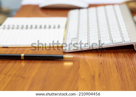 Blank notebook with keyboard and pen on wooden office table