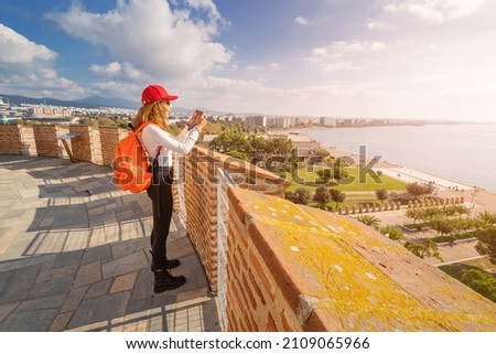 Happy tourist woman taking picture while stands on the White Tower viewpoint and enjoys the panorama of Thessaloniki city in Greece