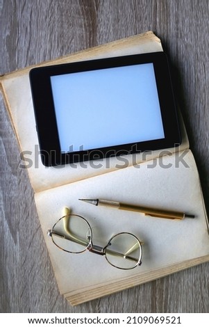 Open book, reading glasses, golden mechanical pencil and e-reader device on the table. Top view.