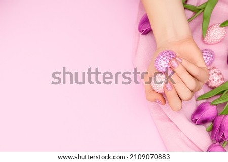 Female hand with glitter purple nail design. Female hand hold easter eggs decorated with purple and pink gems. Model hand with spring nail design on purple background. Copy space. Royalty-Free Stock Photo #2109070883