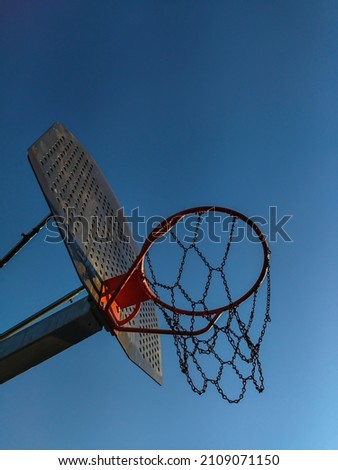 Orange basketball basket seen from below with rusty metal net and blue sky in the background