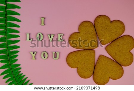 inscription I love you on a pink background. top view of wooden letters and heart shaped gingerbread, asthenia green branch, valentine's day concept