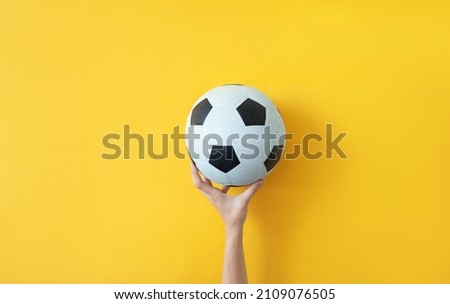 Female hand holding soccer ball on yellow background Concept photo