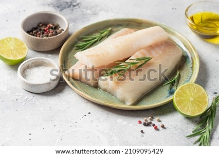 Ceramic plate with fresh raw cod fish, aromatic herbs, spices, lime and olive oil on kitchen table. copy space