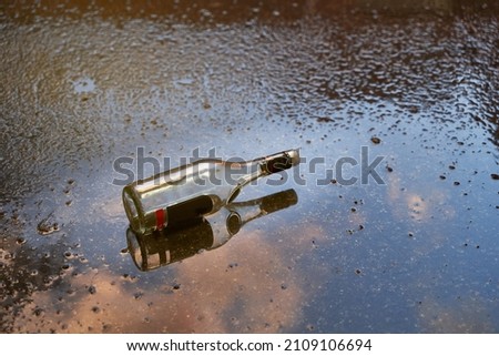Alcoholism problem concept. Empty bottle of liquor on a wet floor after rain at sunset Royalty-Free Stock Photo #2109106694