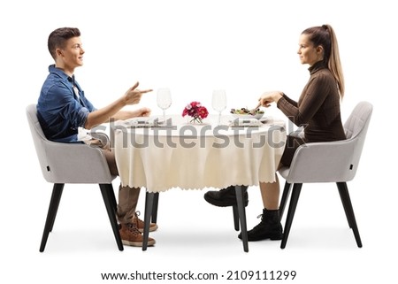 Profile shot of a casual young man and woman sitting at a restaurant table and talking isolated on white background Royalty-Free Stock Photo #2109111299
