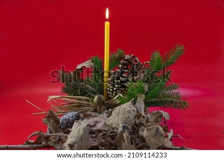 Orthodox Christmas decoration, burning candle in basket with pine tree, oak tree leaves, pine cone on red background