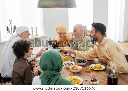 young arabian man talking to cheerful multicultural muslim family during dinner Royalty-Free Stock Photo #2109116576