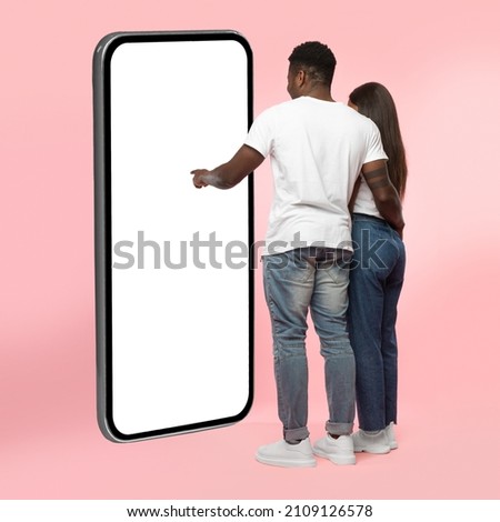 Rear Back View Of Black Couple Using Big Smartphone With Blank White Screen Touching Huge Display Panel With Finger, Guy Higging Lady Standing On Pink Background, Mock Up. Full Body Length Royalty-Free Stock Photo #2109126578