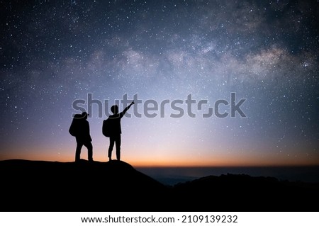 Silhouette of young couple traveler and backpacker standing and watched the star and milky way on top of the mountain. He enjoyed traveling and was successful when he reached the summit. Royalty-Free Stock Photo #2109139232