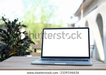 Mockup laptop computer with empty screen on wooden table at outdoor. Blank screen for your advertising text.