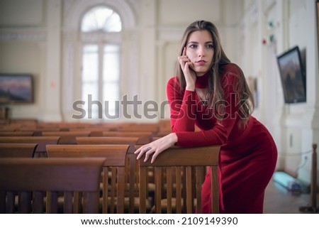 Young girl in the red dress stands near the chair in the art museum hall.