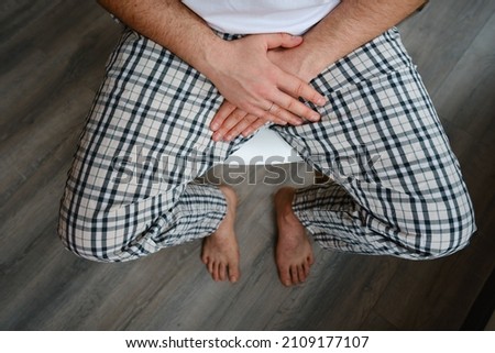 A man grabs and covers his crotch with his hand while sitting on a chair. Health diagnostics. Мedical examination Royalty-Free Stock Photo #2109177107