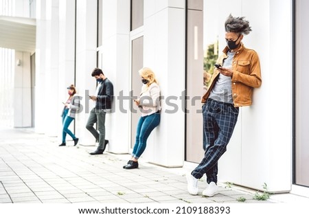 People using cell phones covered by mask at omicron variant wave - Bored men and women looking for news on mobile devices - College students breaking at university place building - Focus on right guy Royalty-Free Stock Photo #2109188393
