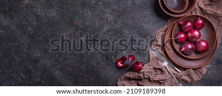 Ripe red onion bulbs in a clay bowl on a stone surface, horizontal banner, flat lay, low key photography with free copy space for text