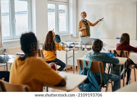 Happy elementary teacher explaining math lesson on whiteboard to her students during a class.  Royalty-Free Stock Photo #2109193706
