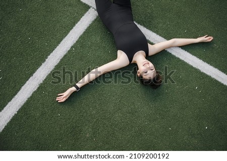 a Caucasian woman is resting after sports. A woman is lying on artificial grass in a park, on a sports field. A tired young woman is resting after a run in the fresh air.