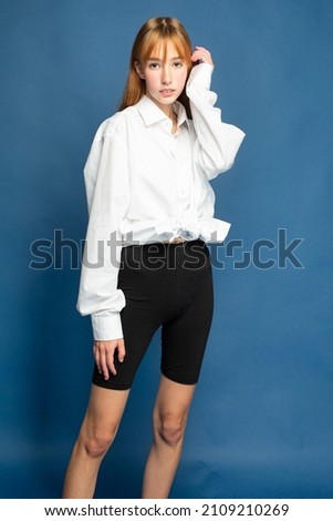 Standing girl with red hair and white skin isolated on blue in black shorts