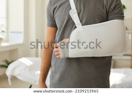 Closeup crop of injured man wear sling on broken leg. Unwell guy with protective bandage gear on arm, have injury or trauma. Rehabilitation concept. Healthcare and medicine. Health insurance cover. Royalty-Free Stock Photo #2109213965