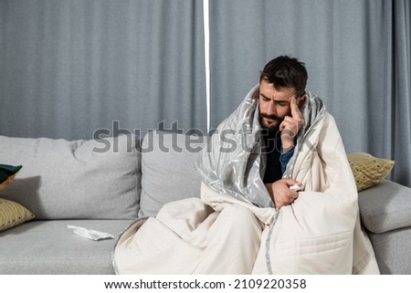 Young ill man coming early from the work to home feeling sick and exhausted. Drunk male sitting on sofa feeling hangover after last night party. Royalty-Free Stock Photo #2109220358